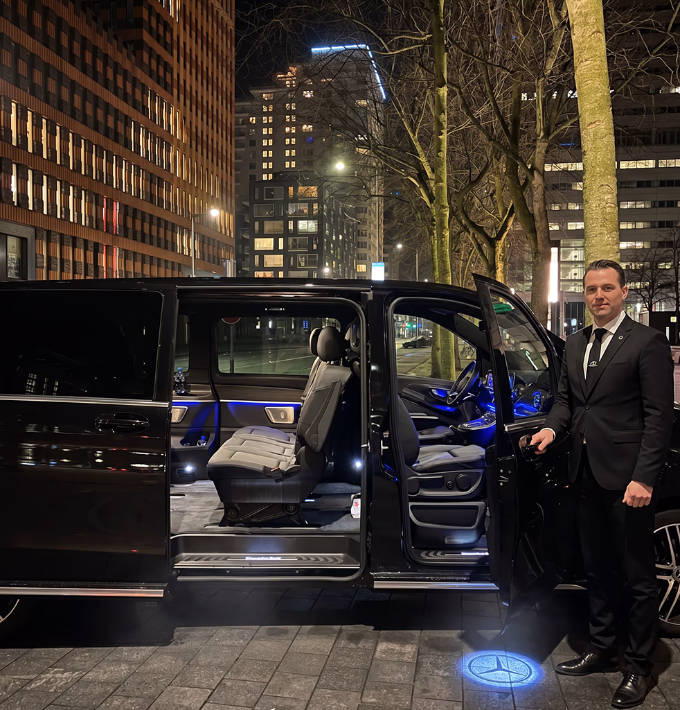 Toursnl private chauffeur in a black suit opening the door of a luxury Mercedes V-Class van at night in Amsterdam