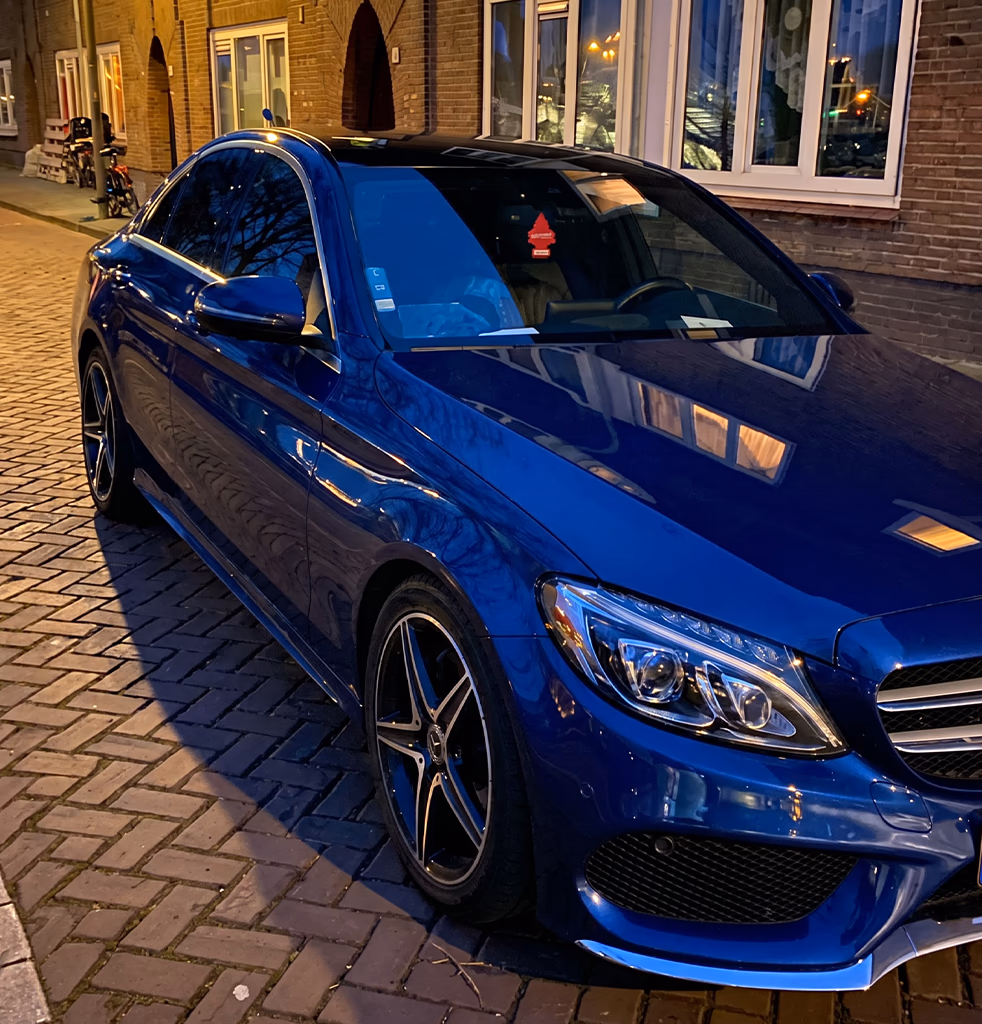 Blue Mercedes C-Class taxi parked on a cobblestone street in central Amsterdam at dusk