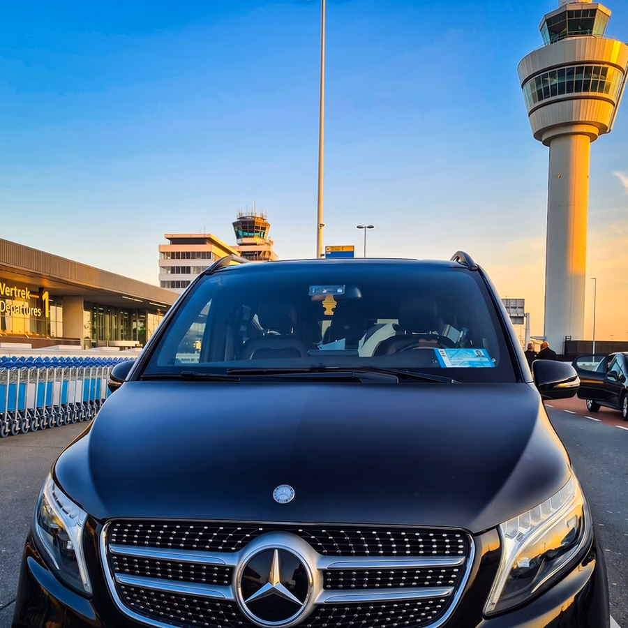 Black Mercedes V-Class chauffeur van at Amsterdam Schiphol Departures 1 at sunset